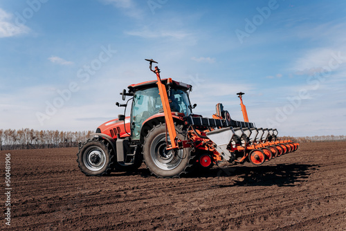 Spring sowing season. Farmer with a tractor sows corn seeds on his field. Planting corn with trailed planter. Farming seeding. The concept of agriculture and agricultural machinery. photo