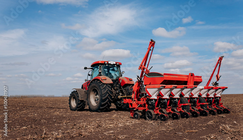 Spring sowing season. Farmer with a tractor sows corn seeds on his field. Planting corn with trailed planter. Farming seeding. The concept of agriculture and agricultural machinery.