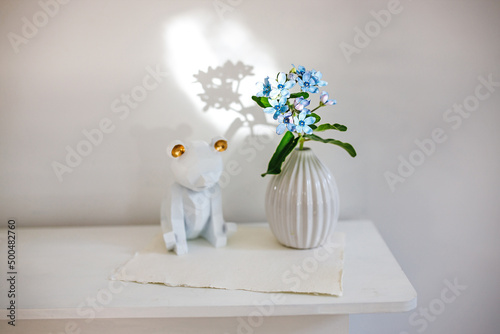 Flower hackelia velutina in a white fluted vase in the style of the seventies, a figurine of bear. Scandinavian style. Shadow photo