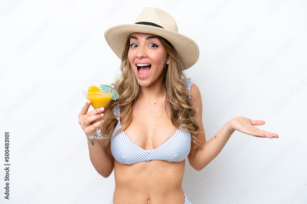 Young woman holding cocktail and wearing a bikini isolated on white background with shocked facial expression