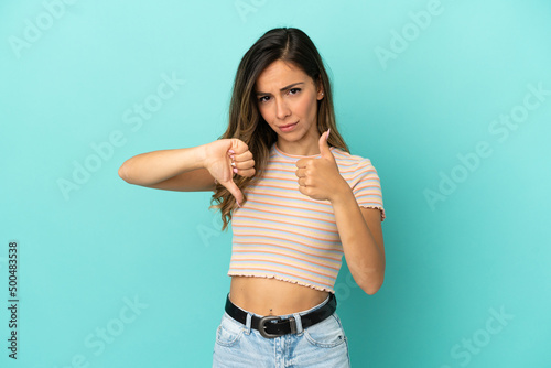 Young woman over isolated blue background making good-bad sign. Undecided between yes or not