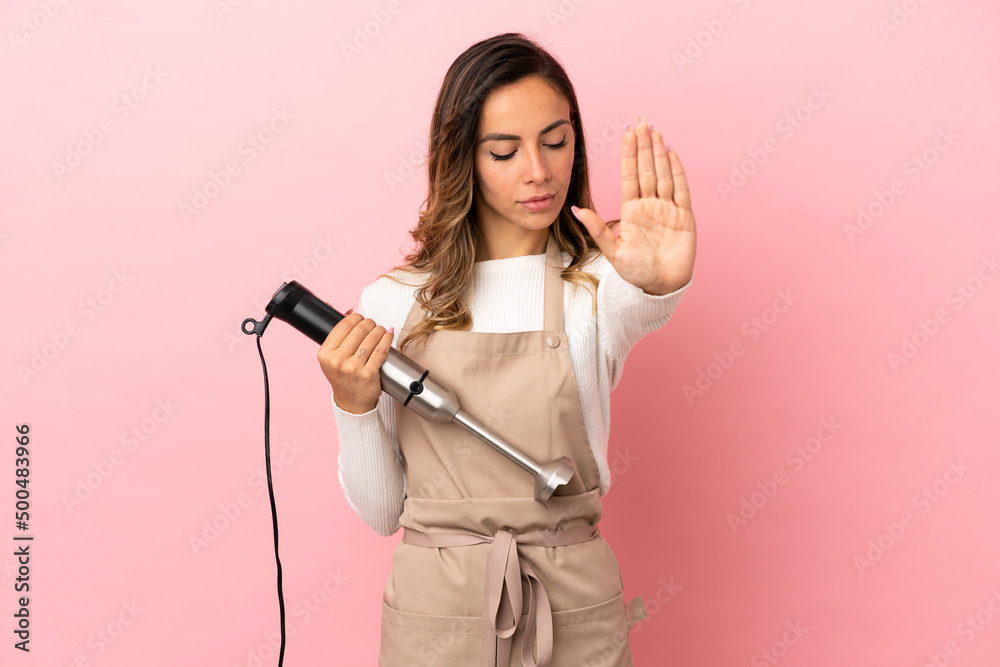 Young woman using hand blender over isolated pink background making stop gesture and disappointed Young woman using hand blender over isolated pink background making stop gesture and disappointed