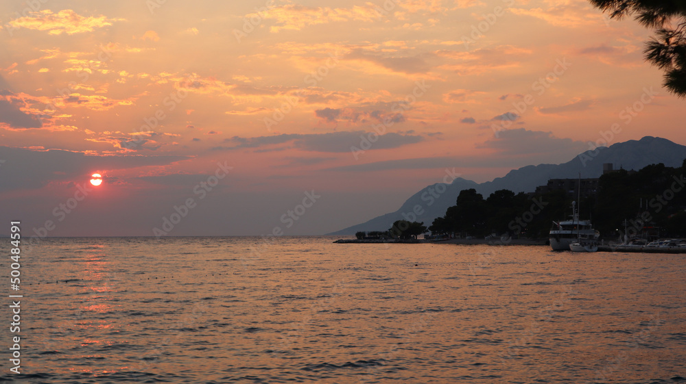 Sunset on the sea coast, bright sun over the sea on the horizon, Brela, Croatia