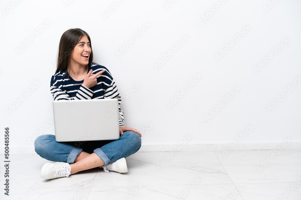 Young caucasian woman with a laptop sitting on the floor isolated on white background pointing finger to the side and presenting a product Young caucasian woman with a laptop sitting on the floor isolated on white background pointing finger to the side and presenting a product