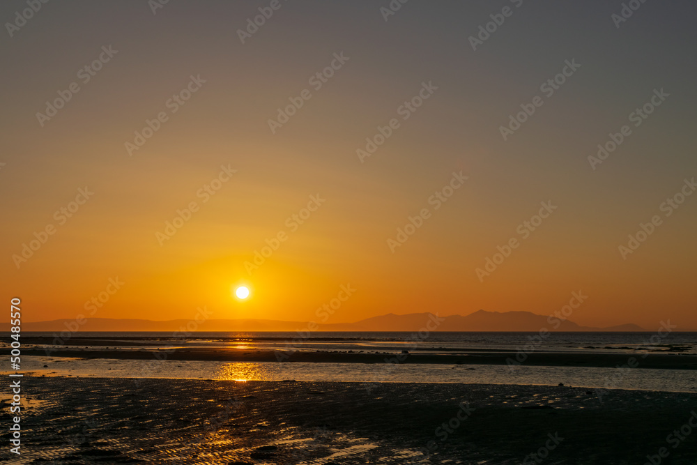 Sunset over the beach and mountain, horizon line yellow and orange shading reflection to water and sand. Focusing at surface shadow. Landscape nature scenery background.