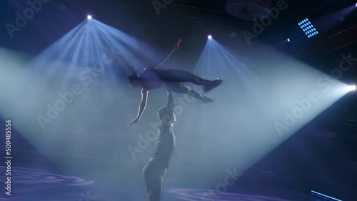 Figure skaters pair perform stationary rotational overhead lift. Man rotates woman high up in the air on one straight hand,her legs and arms outstretched.Risky forbidden support,slow motion,close-up.