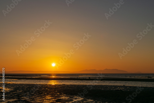 Sunset over the beach and mountain, horizon line yellow and orange shading reflection to water and sand. Focusing at surface shadow. Landscape nature scenery background.