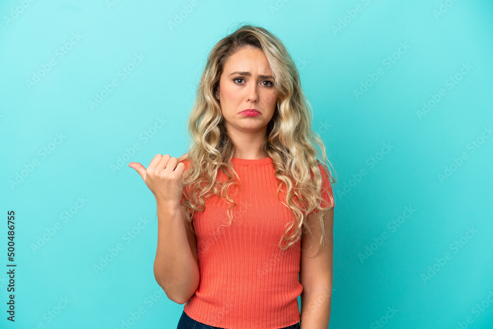 Young Brazilian woman isolated on blue background unhappy and pointing to the side Young Brazilian woman isolated on blue background unhappy and pointing to the side