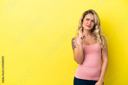 Young Brazilian woman isolated on yellow background with fingers crossing and wishing the best