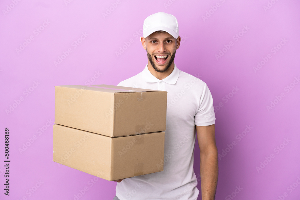 Delivery caucasian man isolated on purple background with surprise facial expression Delivery caucasian man isolated on purple background with surprise facial expression