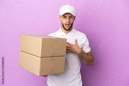 Delivery caucasian man isolated on purple background surprised and shocked while looking right