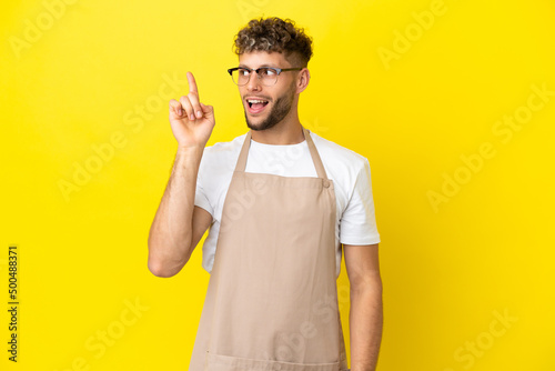 Restaurant waiter blonde man isolated on yellow background intending to realizes the solution while lifting a finger up