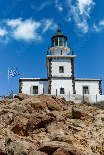 Old lighthouse with Greece flag on blue sky background.