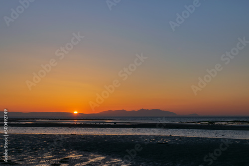 Sunset over the beach and mountain, horizon line yellow and orange shading reflection to water and sand. Focusing at surface shadow. Landscape nature scenery background.