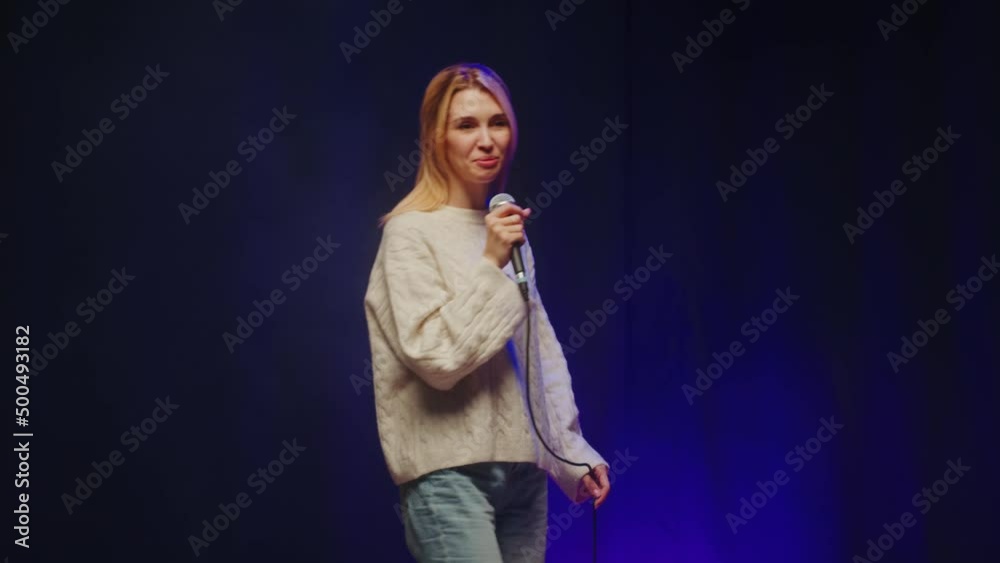 Stand-up cafe, comedy concert. Woman telling jokes on stage. Female comedian speaking with audience using microphone, humorous monologue. Mentor coach training. Stand-up cafe, comedy concert. Woman telling jokes on stage. Female comedian speaking with audience using microphone, humorous monologue. Mentor coach training.