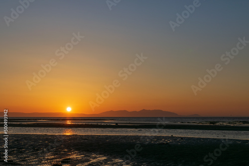 Sunset over the beach and mountain, horizon line yellow and orange shading reflection to water and sand. Focusing at surface shadow. Landscape nature scenery background.