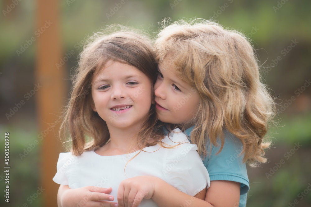 Two little children hug and kiss each other in summer garden. Kids couple in love. Friendship and childhood. Two little children hug and kiss each other in summer garden. Kids couple in love. Friendship and childhood.