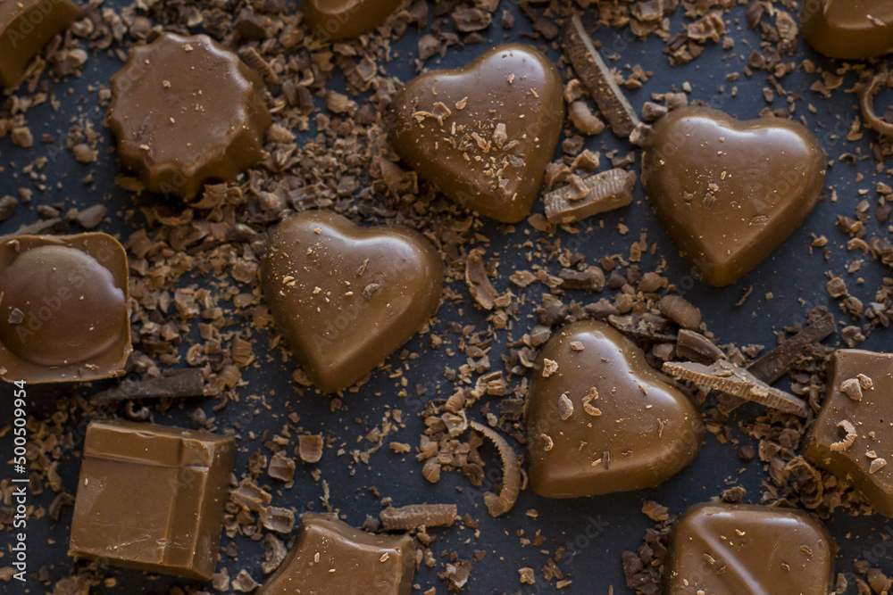Heart shaped chocolates with grated chocolate pieces on black surface,above view