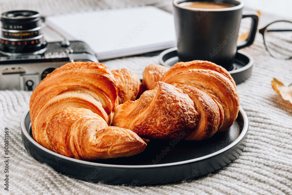 Fresh croissant and cup of coffee on a gray knitted background. Cozy autumn morning breakfast composition Fresh croissant and cup of coffee on a gray knitted background. Cozy autumn morning breakfast composition