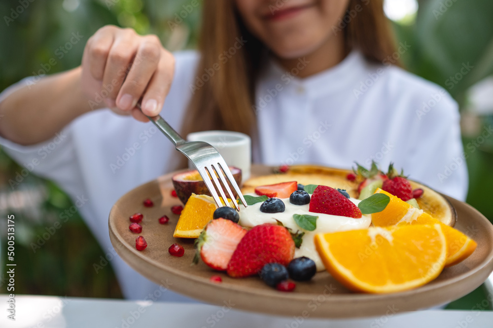 Closeup of a young woman holding and eating mixed fruits french toast brunch in restaurant Closeup of a young woman holding and eating mixed fruits french toast brunch in restaurant
