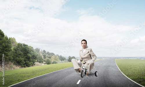 Caucasian woman riding kid's bicycle on road