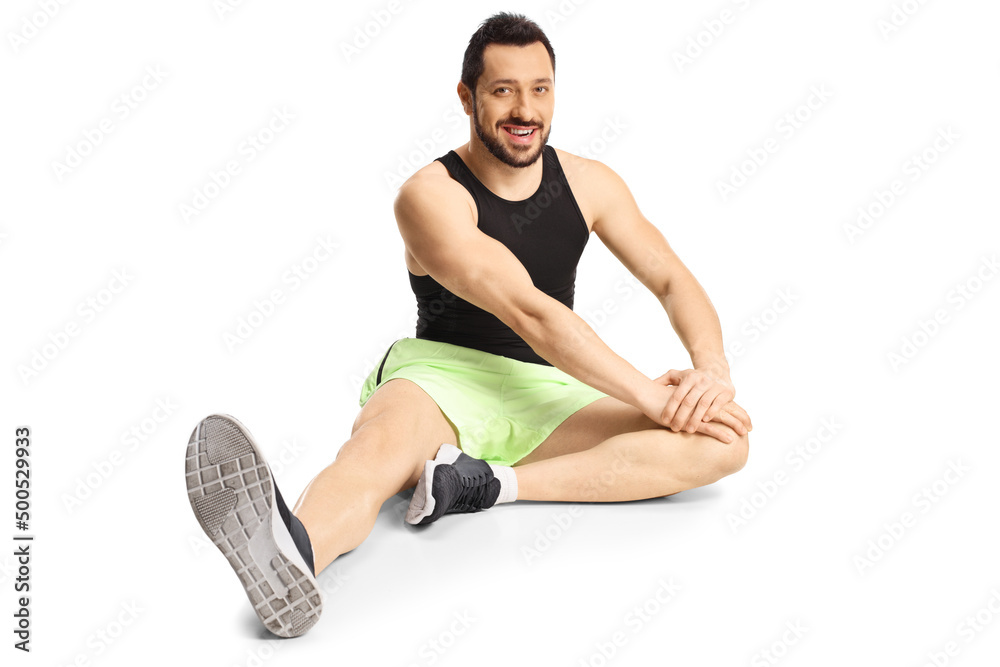 Young man in sportswear sitting on floor stretching his leg Young man in sportswear sitting on floor stretching his leg
