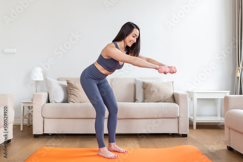 Asian woman exercise with dumbbells at home. Happy female doing arm workout using dumbbells