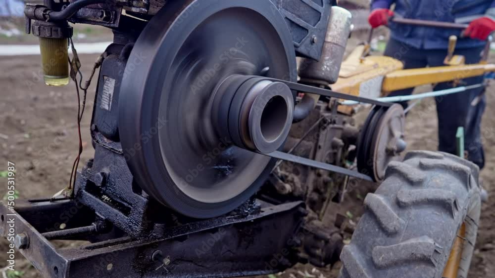 Working process of rotating pulley with belt. Man works in garden with motorized unit motoblock - type of small-sized tractor. Working process of rotating pulley with belt. Man works in garden with motorized unit motoblock - type of small-sized tractor.