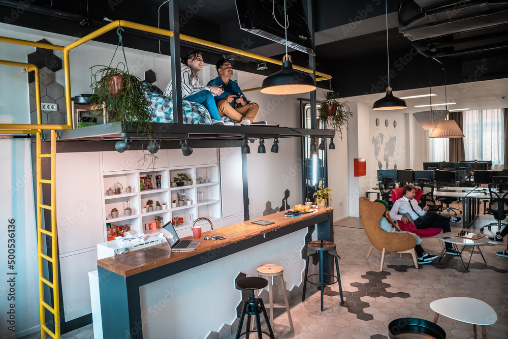 Group of casual multiethnic business people taking break from the work doing different things while enjoying free time in relaxation area at modern open plan startup office