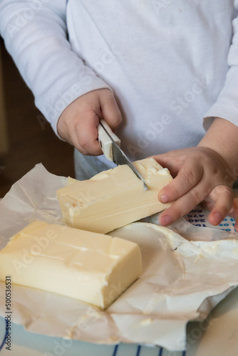 Small children's hands cut butter with a knife on the table and take a piece of butter with their hand
