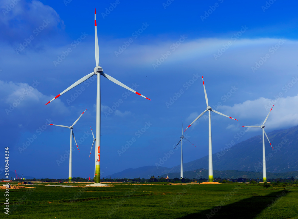 Wind turbine towers in a green field under the blue sky generating alternative energy for sustainable growth. Reducing climate change and global warming 
