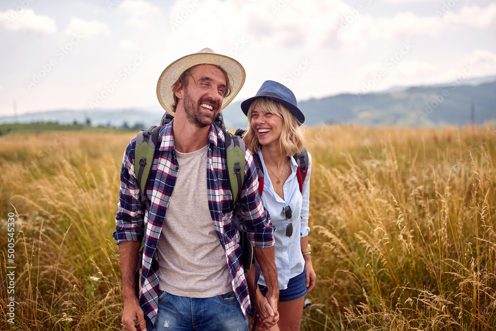 A young couple is in a good mood while walking a meadow. Hiking, nature, relationship, together