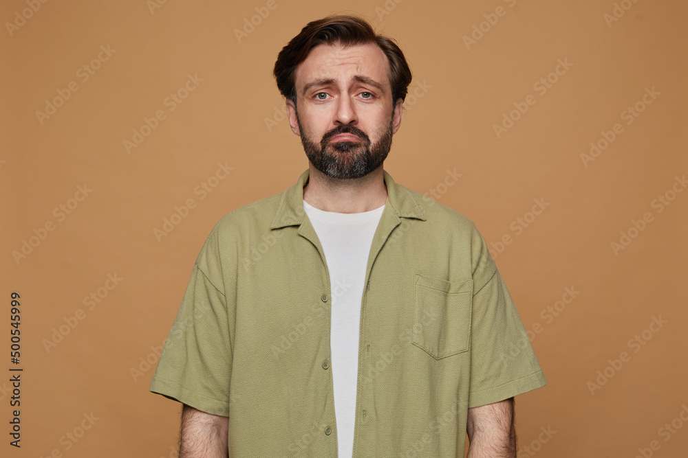 Fototapeta premium studio portrait of bearded man posing over beige background looking into camera with sad, depressed facial expression