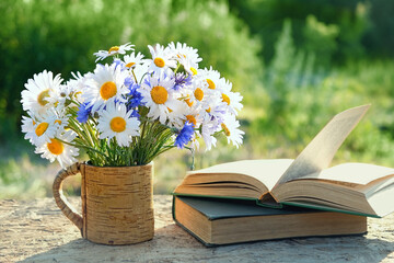 flowers bouqet in cup and old books on table in garden. rustic summer natural background. concept of reading, relaxation. summer season