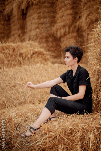 sexy girl in a black jumpsuit on a field in the hay