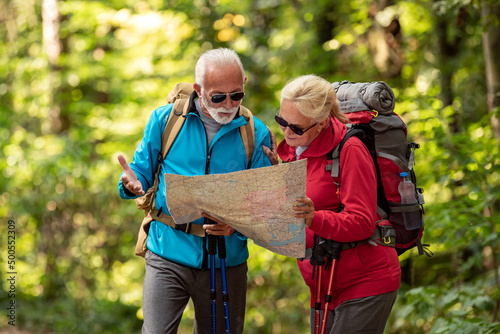 Happy senior couple of tourists looking at map in forest