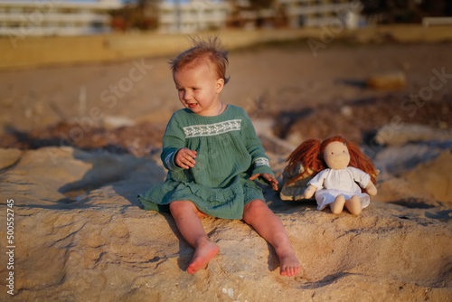 Girl baby toddler in a dress plays on the seashore sunset, lifestyle