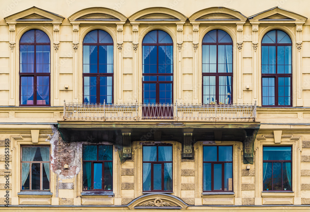 Fototapeta premium Balcony and many windows in a row on the facade of the urban historic apartment building front view, Saint Petersburg, Russia 
