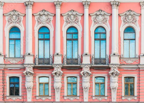 Atlantes and many windows in a row on the facade of the urban historic apartment building front view, Saint Petersburg, Russia

