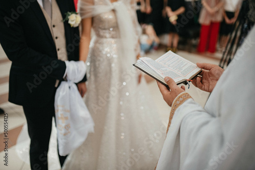 Wedding matrimony in church. Priest putting on golden wedding ring on bride finger. Wedding candles.