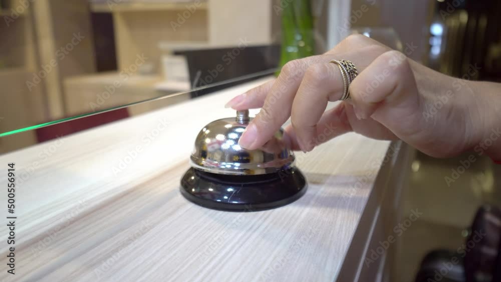 A woman's manicured hand rings the bell at the hotel reception. The metal bell reflects the Georgian flag or the red and white flag. The tourist's hand hits the bell at the hotel. A woman's manicured hand rings the bell at the hotel reception. The metal bell reflects the Georgian flag or the red and white flag. The tourist's hand hits the bell at the hotel.