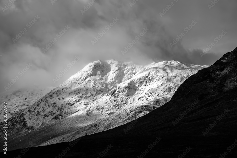 Black and white Majestic beautiful Winter landscape image of Lost Valley in Scotland with snowcapped Buachaile Etive Baeg sand distant mountain range with dramatic sky