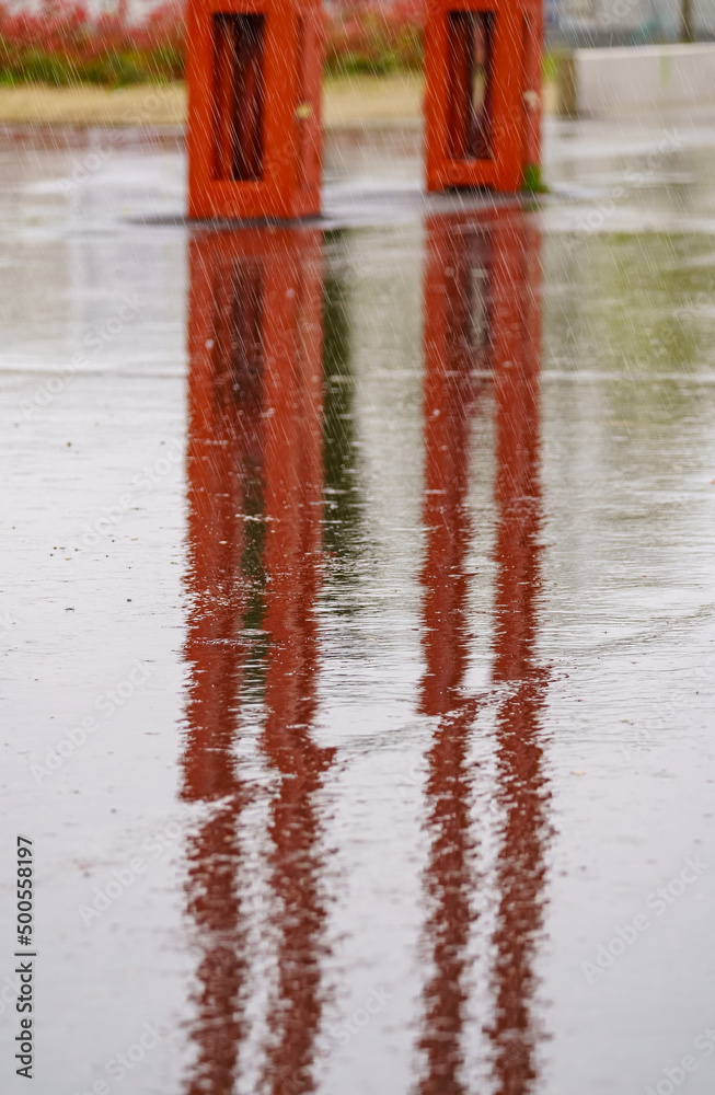 Heavy rain falling on the ground and forming reflections with street furniture. Heavy rain falling on the ground and forming reflections with street furniture.