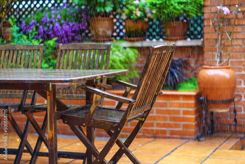 Heavy rain falling on the garden furniture made of teak wood and flowering plants.