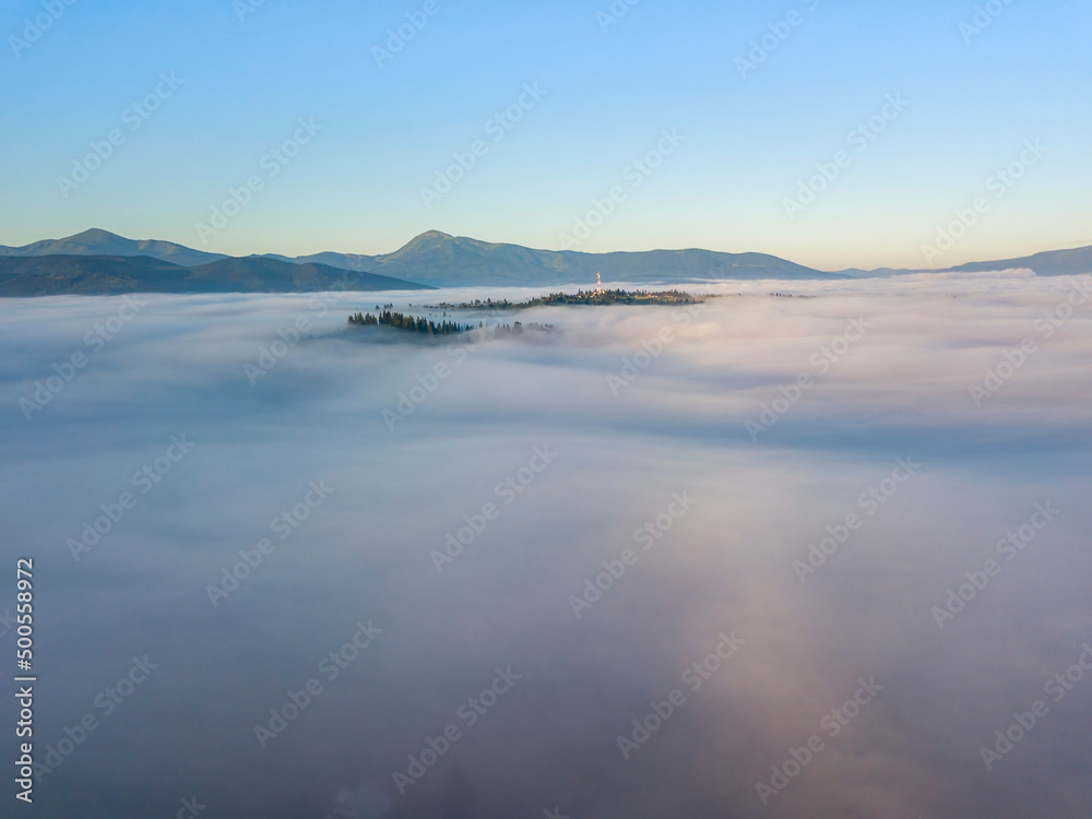 Sunny morning in the foggy Carpathians. A thick layer of fog covers the mountains. Aerial drone view.