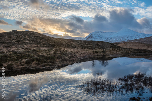 Epic Winter sunset landscape image across Loch Ba in Scottish Highlands towards snow covered mountain range in distance photo