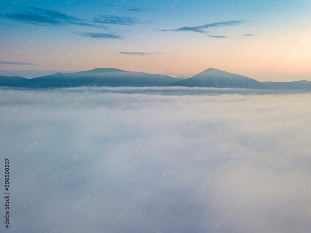 The rays of dawn over the fog in the Ukrainian Carpathians. Aerial drone view.