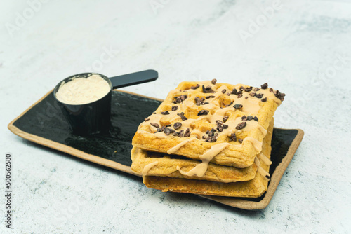 Waffle with chocolate and peanut butter and protein powder on a black plate on white background