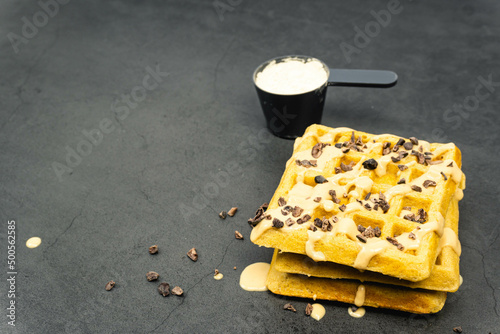 Protein waffles and powder with peanut butter and chocolate chips on dark background. Copy space.