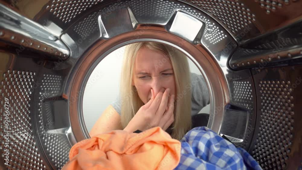 Smelly washing machine and laundry room. Young blonde woman looks